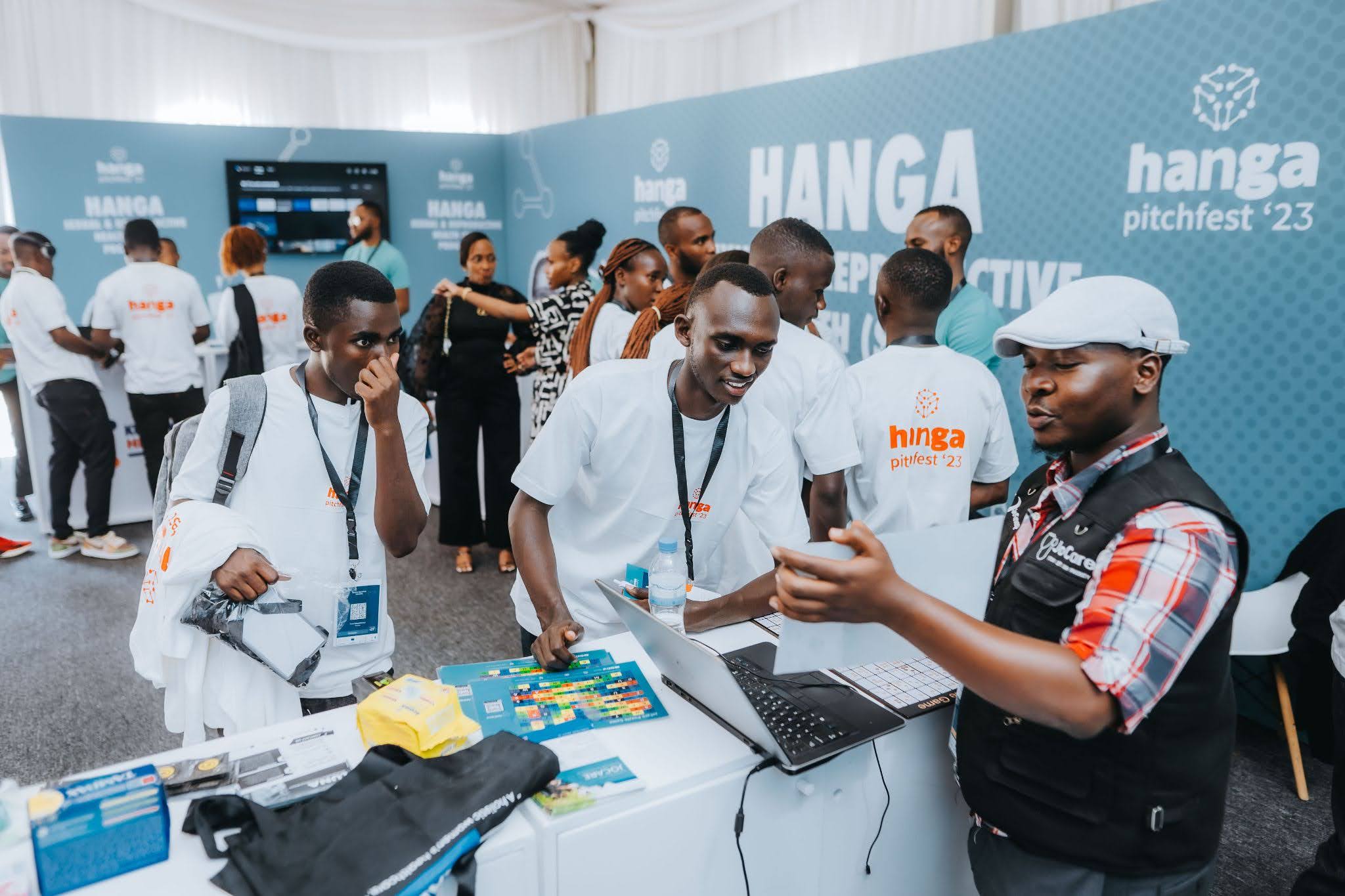 People at the Hanga Pitchfest '23 event, some in white Hanga t-shirts, gathered around a laptop and booths