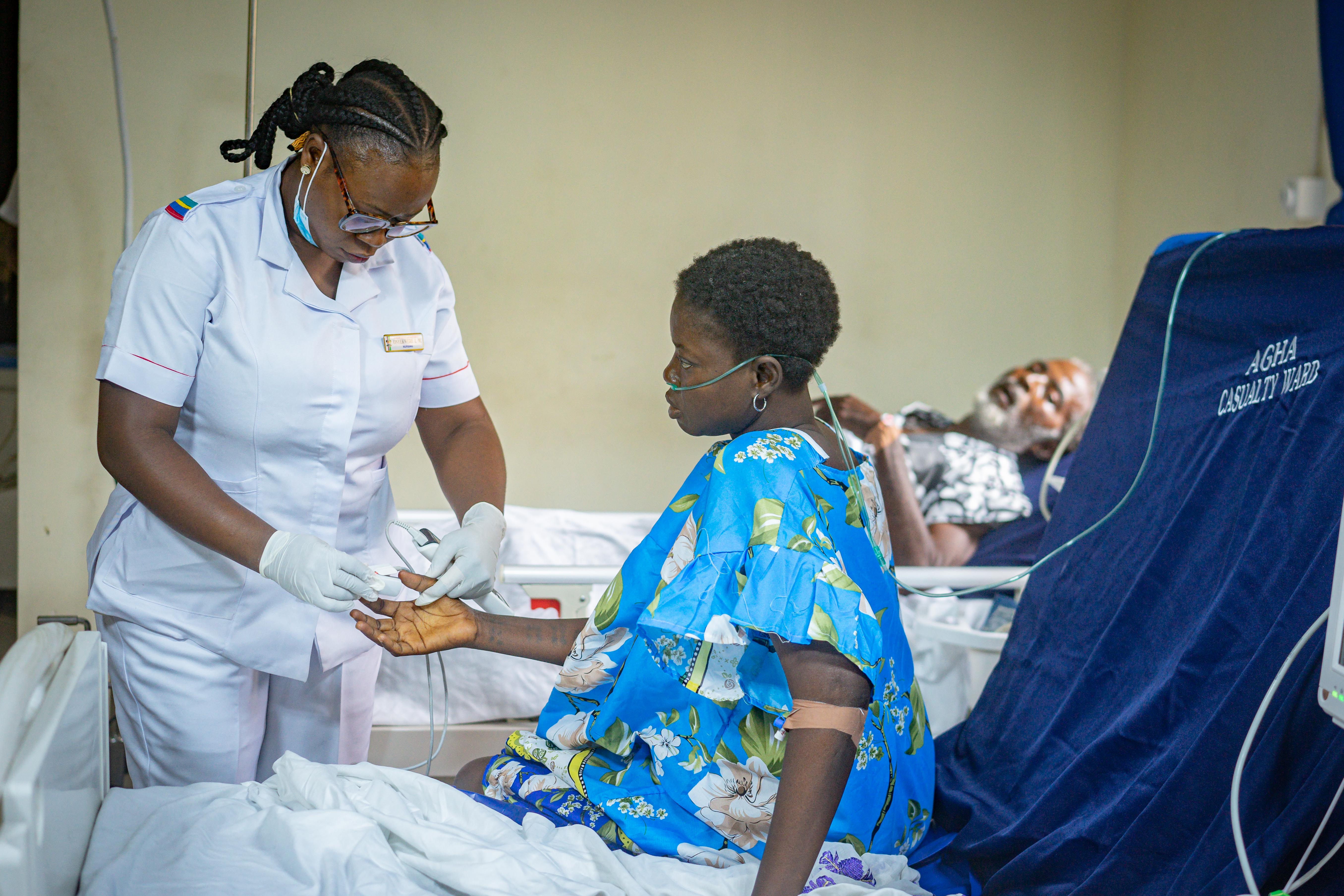 A nurse checking the pulse of a seated patient wearing an oxygen tube in a hospital ward